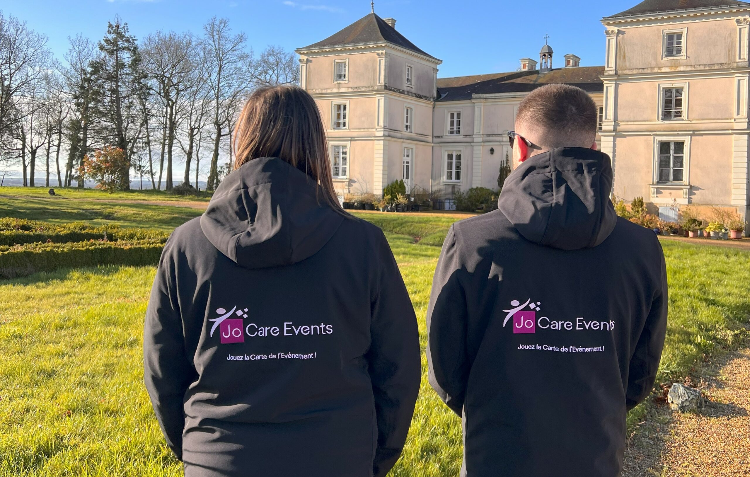 Deux membres de l'équipe se tiennent debout, dos à la caméra, pour montrer le logo de l'agence événementielle sur le dos de leurs vestes.